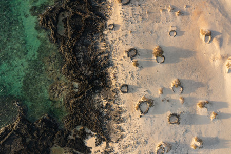 Scenic aerial view of Los Charcos Beach featuring traditional stone wind shelters along the...