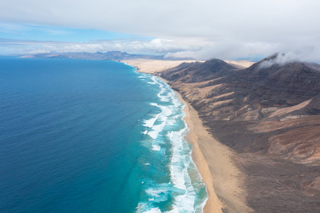 Breathtaking bird's-eye view of Cofete's long sandy beach with the cloud-covered mountains of...