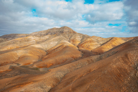 Aerial view of the rugged mountains of Fuerteventura, featuring isolated houses surrounded by vast volcanic landscapes and golden light at sunset. Peaceful, remote, and cinematic scenery.の写真素材
