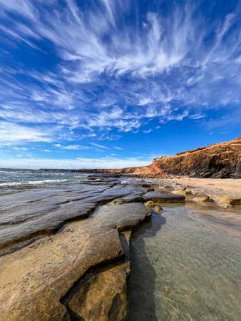 Majestic view of Playa de Los Ojos in Fuerteventura, where rugged volcanic rocks meet the deep blue Atlantic Ocean. The textures of the coastline and the powerful waves create a sense of wild, untouched beauty typical of the Canary Islands.の写真素材