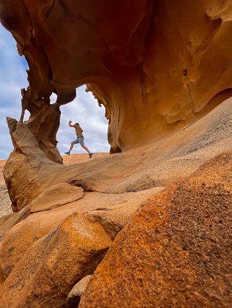 A man jumping joyfully in front of the iconic natural rock arch of Las PeÃ±itas, Fuerteventura, under a bright blue sky. Adventure and freedom in the Canary Islands.の写真素材