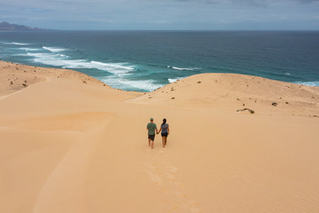 A romantic scene of a couple strolling hand in hand across the golden sand dunes of JandÃ­a,...