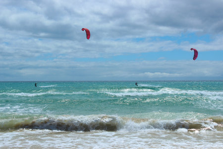 Sunny day at Sotavento Beach, Fuerteventura, with kitesurfers performing dynamic maneuvers on the waves. Perfect for illustrating adventure, sports, and coastal lifestyle in high-quality imagery.の写真素材