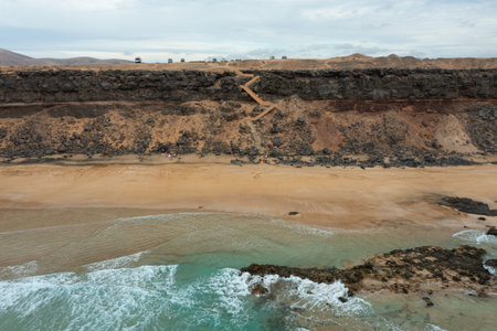 Drone shot capturing the remote and untouched beauty of Playa de las Escaleras, a hidden beach surrounded by rugged coastal landscapes in Fuerteventura.の写真素材