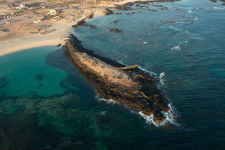 Drone aerial view of La Concha Beach lagoon and natural volcanic rock breakwater at sunset in El Cotillo, Fuerteventura. Turquoise shallow waters meet deep Atlantic blue under warm golden hour light in the Canary Islands.の写真素材