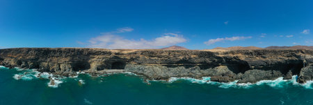 Aerial drone view of the rugged coastline and black sand beach surrounding the Ajuy Caves in...