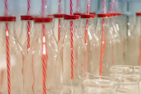 Empty glass bottles for water, liquid food, smoothies with red lids with holes for tubes and with red striped tubes. Close up, blured backgroundの写真素材