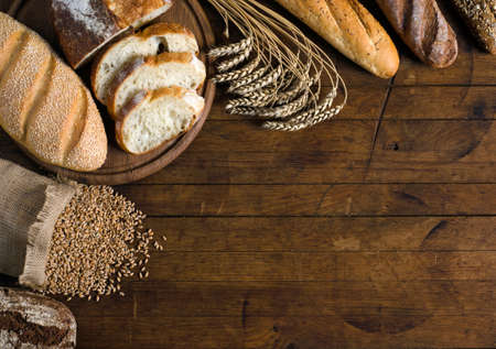 Assortment of bread, ears and grains of wheat on wooden table with copy space for your text. Rustic style, top view.の写真素材