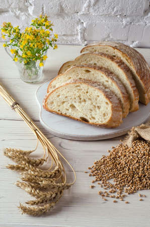 Sliced bread on  cutting board and spikelets of wheat on background of white wall. Rustic style, top view.の写真素材