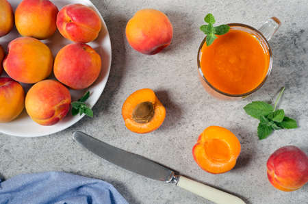 Apricot smoothies in a glass cup and fresh apricots with mint leaves on a gray textured background. Top view.の写真素材