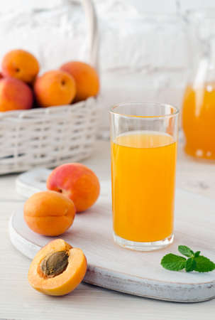 Apricot juice in glass on the kitchen board and ripe apricots in basket on background of white brick wall. Close-up.の写真素材