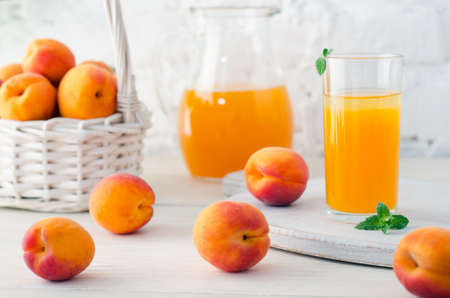 Apricot juice in glass and decanter with ripe apricots on wooden table on background of white brick wall. Close-up.の写真素材