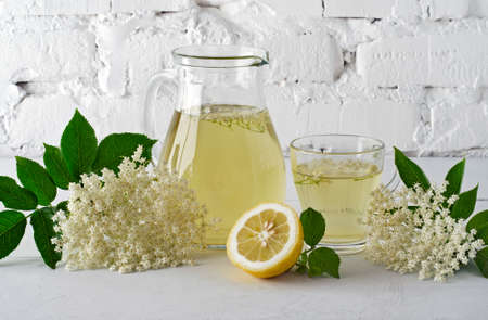Drink from elderberry flowers in carafe with slice of lemon against  white brick wall.の写真素材