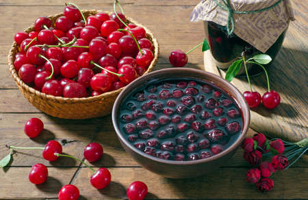 Cherry jam in a clay bowl and red ripe cherries in a basket on a wooden table. Rustic style.の写真素材
