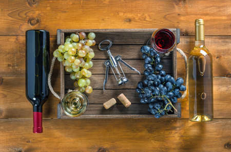 Two bottles of wine and bunch of grapes in box with glasses of wine and corkscrew on wooden background. Top view, copy-space.の写真素材