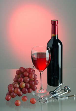 Glass of red wine, brush of red grapes, bottle of wine and metal corkscrew on colored background. Backlight. Copy-space.の写真素材
