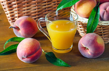 Peach juice in a glass beaker and ripe peaches on a wooden table. Rustic style.の写真素材