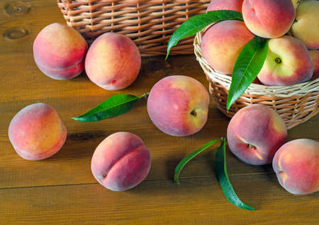 Juicy peaches with green leaves on a wooden table. Rustic style.