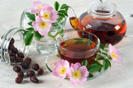Rosehip flowers and cup of tea with rosehips on white wooden table. Ð¡lose up.の写真素材