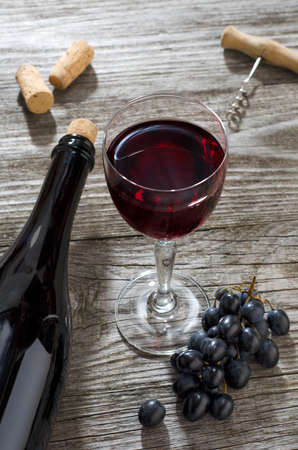 Glass of red wine, bottle of wine, bunch of blue grapes and corkscrew on gray wooden table.の写真素材