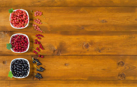 Ripe berries of pink, black and red currants in plates on a wooden table. Top view, copy-space.の写真素材