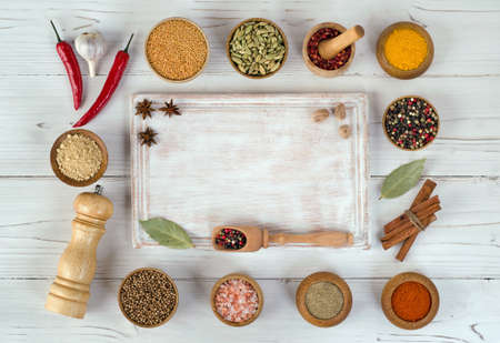 Variety of herbs and spices around an empty cutting board on white wooden background. Top view. Flat lay.の写真素材