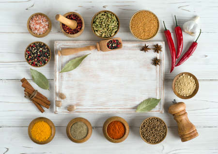 Set of various spices and herbs around an empty cutting board on white wooden background. Top view copy space. Flat lay