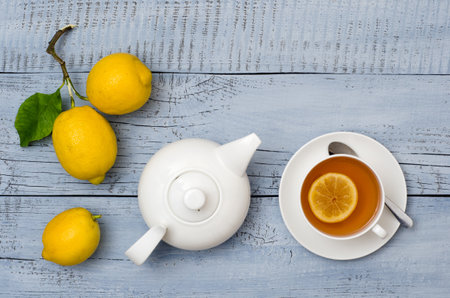 Top view of cup of tea, ripe lemons and teapot on light blue wooden background with copy space for your text.の写真素材