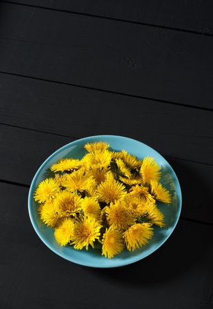 Top view on yellow dandelionsin blue plate on dark wooden background.の写真素材