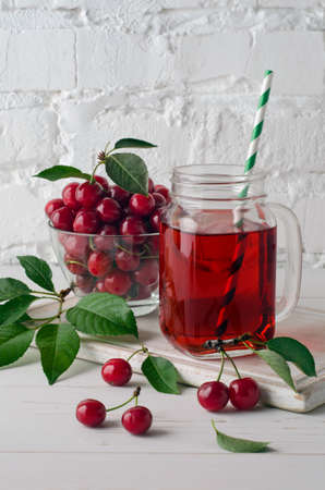 Cherry juice in a glass mason jar and cherry berries on white brick wall background. Ð¡lose-up.の写真素材