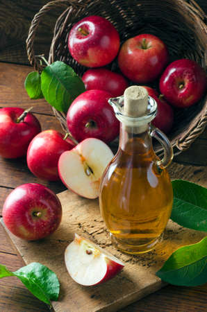 Apple cider vinegar in glass bottle and wicker basket with fresh apples on wooden background. Rustic style. Healthy organic food.の写真素材