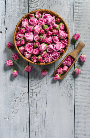 Top view of basket and wooden scoop with fresh tea rose buds on a light blue wooden background with copy space for your text.の写真素材