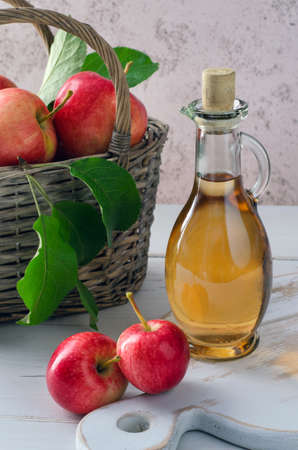 Apple cider vinegar in glass bottle and ripe apples in basket on white wooden table. Healthy organic food.の写真素材