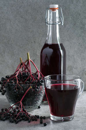 Elderberry syrup in glass bottle and cup, ripe berries on gray stone background. Ð¡lose-up.の写真素材