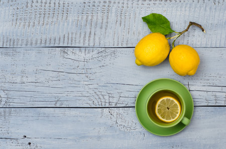 Two ripe lemons and green cup of tea on blue wooden background with copy space for your text. Top view.の写真素材