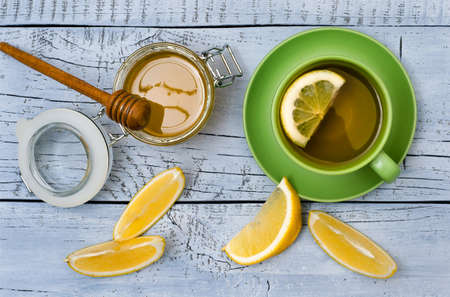 Top view on a green cup of tea with lemon, honey and teapot on light blue wooden backdropの写真素材
