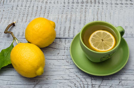 Two ripe lemons and green cup of tea on light blue wooden background. Ð¡lose-up.の写真素材