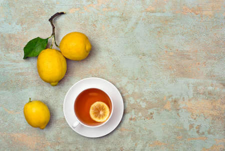 Top view on three ripe lemons and cup of tea on multicolored textured background with copy space for your text.の写真素材