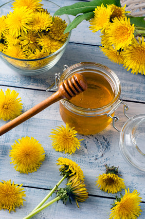Homemade dandelion honey in glass jar with fresh yellow flowers on light blue wooden background. Top view.の写真素材