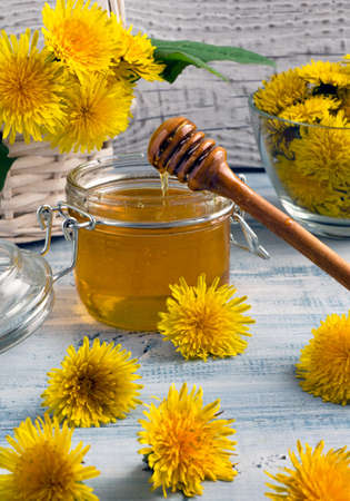 Dandelion honey in glass jar with fresh yellow flowers on light blue wooden background.の写真素材