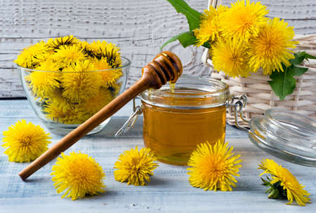 Bright yellow dandelions and homemade dandelionin honey in glass jar with on light blue wooden background. Close-up.の写真素材