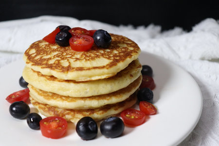 Pancakes with blueberries and cherry tomatoes on a white plateの写真素材
