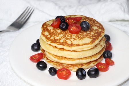 Pancakes with berries and cherry tomatoes on a white plate.の写真素材