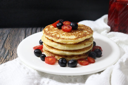 Pancakes with blueberries, cherry tomatoes and honey on a white plateの写真素材