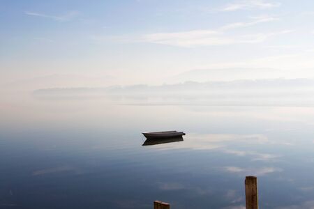Boat on lake with reflection of sky and fogの写真素材