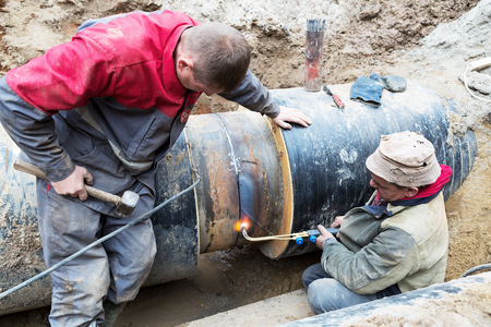 Odessa, Ukraine - October 11, 2016: Repair of heating duct. The workers, welders made by electric welding and gas welding on large iron pipes at a depth of excavated trench.のeditorial素材