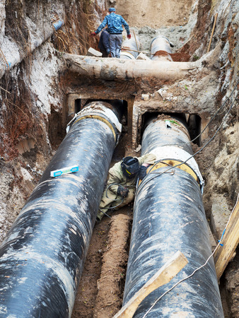 Odessa, Ukraine - October 11, 2016: Repair of heating duct. The workers, welders made by electric welding and gas welding on large iron pipes at a depth of excavated trench.のeditorial素材
