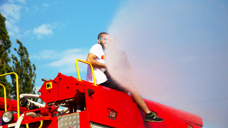 ODESSA, UKRAINE - August 5, 2017: Boys and girls in wet clothes fun to do selfie during festival of Holi. Smiling fireman sitting on fire truck pours water on people from brandsby. Festival Color festのeditorial素材