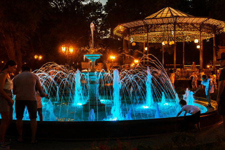 ODESSA, UKRAINE - August 4, 2018: tourists and guests of the city are resting in the city park near the musical colorful fountain in the evening. Light fountain show in a night parkのeditorial素材