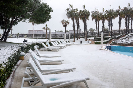 Heavy snowfall on the Mediterranean coast. Snow storm and white covered palm trees. Empty beaches and hotel cafes.のeditorial素材